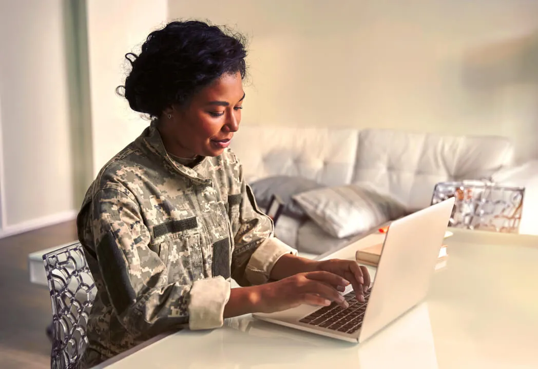 A woman wearing fatigues types on her laptop