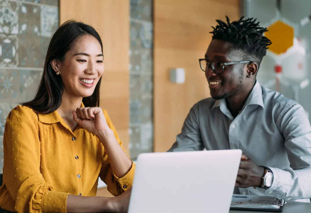 Two smiling individuals collaborate on a laptop, engaged in a productive work session.
